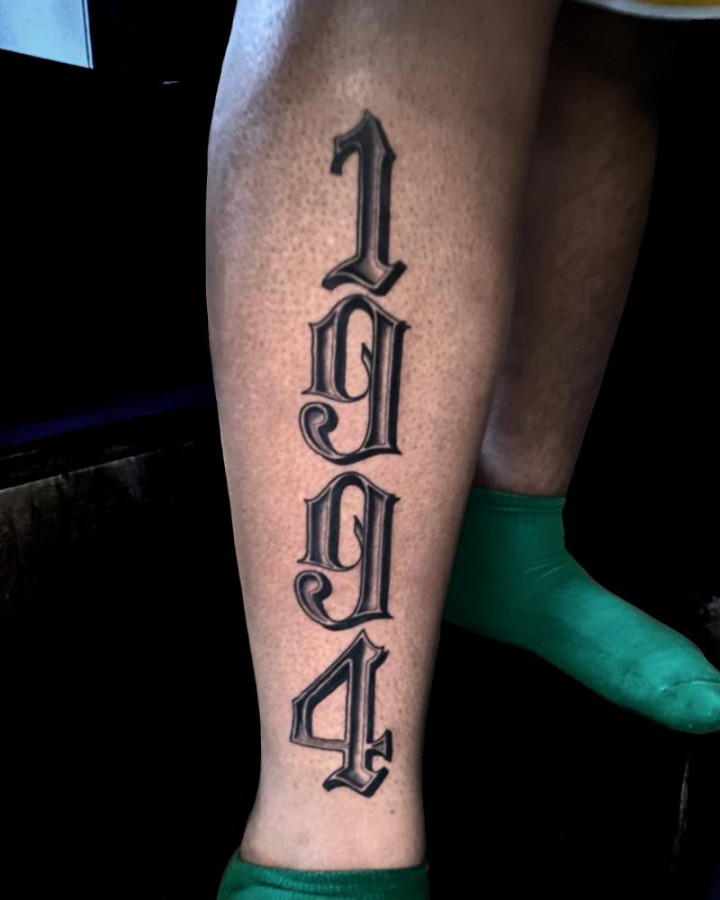 Large "" lettering tattoo located on the shin.